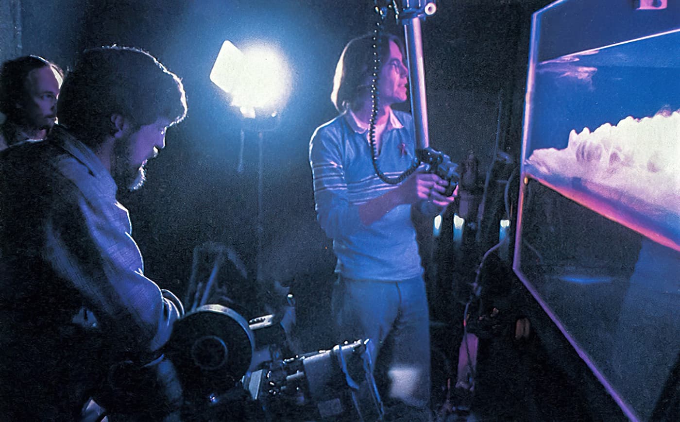 Crew members stand in front of a large aquarium filled with artificial clouds