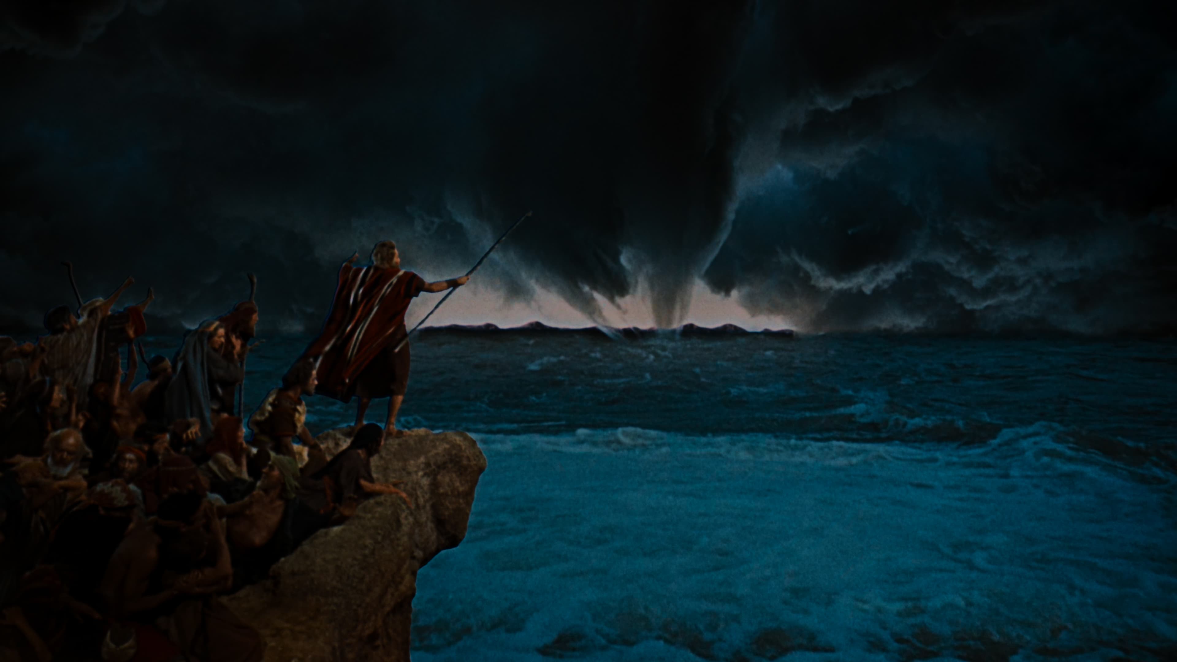 a man standing on the edge of a large rock overlooking the sea with supernatural clouds in the background