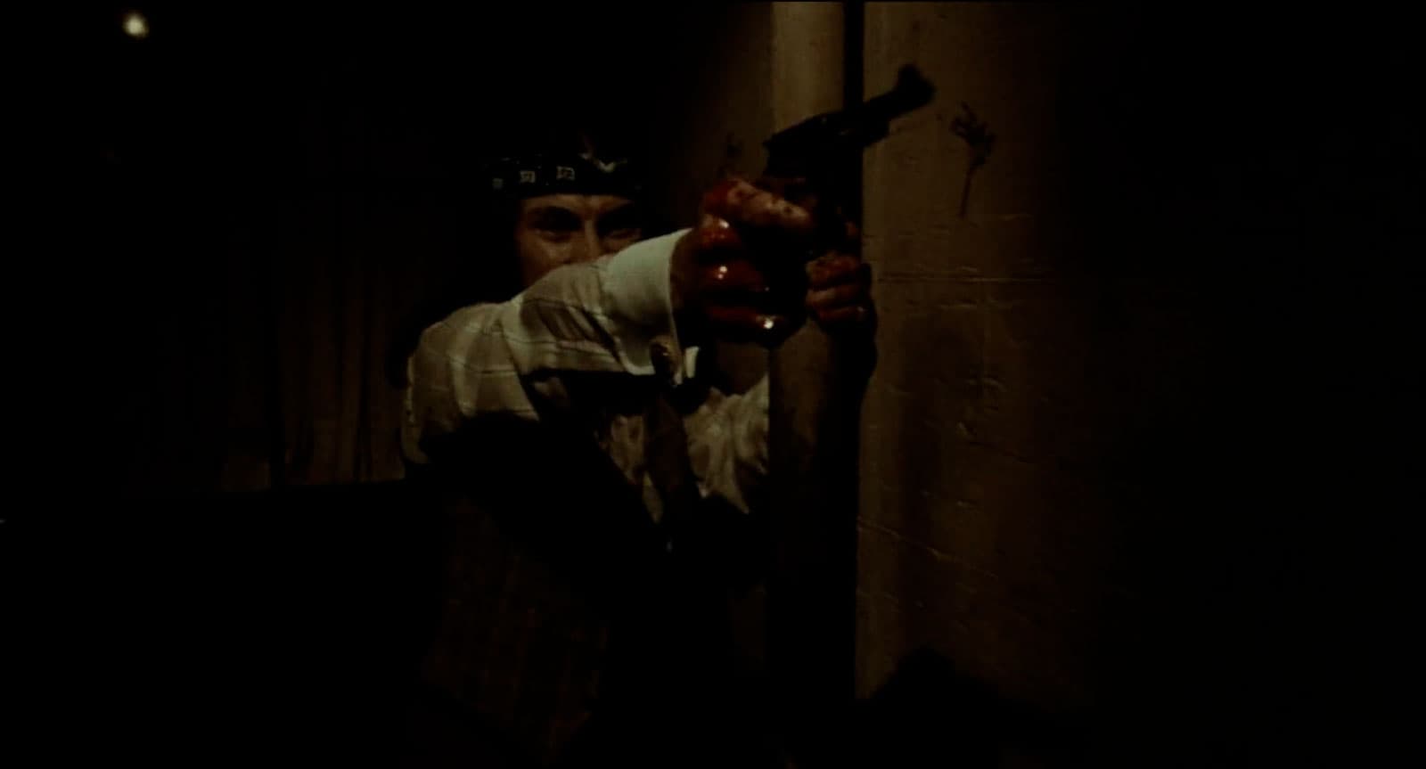 A man aims a gun with blood on his hands